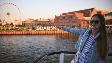 Gdansk Polonya 'da teknede bir kadın Motlawa nehri kıyısı silueti ve dönme dolap ile altın saat yaz seyahati konseptinde