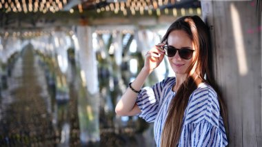 Güneşli bir günde çizgili elbiseli ve güneş gözlüklü şık bir genç kadının portresi.