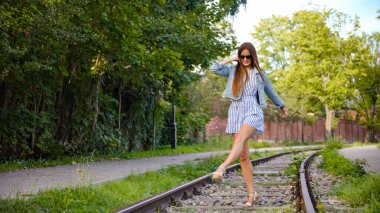 Kaygısız genç kadın güneşli şehir parkında raylarda yalın ayak yürüyor.