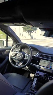 Beverly Hills 'teki otonom Waymo Jaguar I Pace taksisinin arka koltuğundan dikey iç görünüş boş sürücü koltuğu direksiyonu ve navigasyon ekranını gösteriyor.