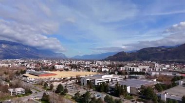 Geniş panoramik drone görüntüsü Grenoble kentsel bölgeler, endüstri evleri ve bulutlu gökyüzü altındaki dağları gösteriyor