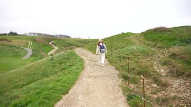 Sırt çantalı bir kadın Etretat Normandiya yakınlarındaki sahil yolunda yokuş yukarı yürüyor.