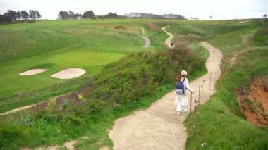 Etretat Normandiya yakınlarındaki yeşil sahil tepesinde bulutlu bahar gökyüzünün altında dolambaçlı toprak yolda yürüyen bir kadın.
