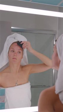 Genç bir kadın, şişkinliği azaltmak ve sabah güzellik rutininde lenfatik drenajı arttırmak için göz altı bölgesinin altına gua sha taşıyla masaj yapıyor.