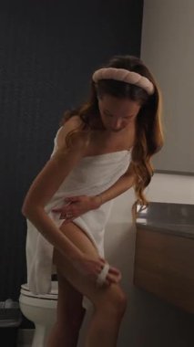 Kadın evde sakin bir vücut bakımı sırasında bacaklarını hafifçe yukarı doğru fırçalar.