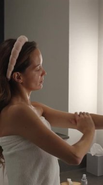 Evde sakin bir vücut bakımı sırasında kadın yavaşça kollarına nemlendirici krem sürüyor.