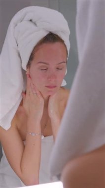 Temizleyiciyi çalkaladıktan sonra ıslak yüzünü ellerle örten genç bir kadın. Sabah güzellik programının bir parçası.