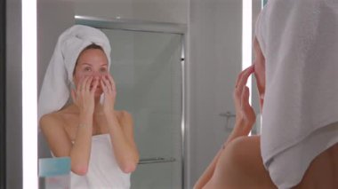 Genç bir kadın yüzüne nemlendirici krem sürüyor ve sağlıklı bir görünüm takınıyor. Sabah güzellik programının bir parçası.