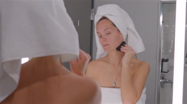 Duştan sonra yüz kremi süren genç bir kadın. Sabah güzellik programının bir parçası.