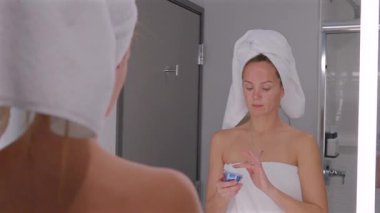 Cilt rengini tazelemek için mavi bir kavanozdan hidratlaştırıcı krem süren bir kadın. Sabah güzellik programının bir parçası.