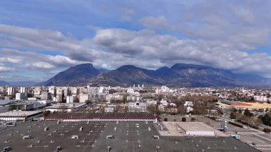 Grenoble 'ın geniş panoramik görüntüsü şehir merkezlerini, endüstrileri ve dağları bulutlu gökyüzünün altında gösteriyor.