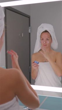 Duştan sonra yüz kremi süren genç bir kadın. Sabah güzellik programının bir parçası.