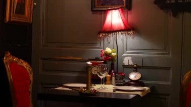 İki kişilik romantik masa. Kırmızı kadife koltuklar, mumlar ve sıcak lamba ışığı.