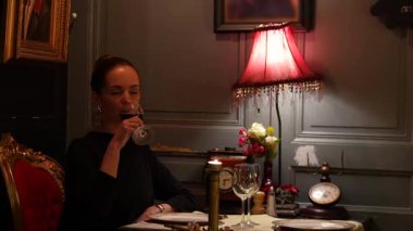 Kırmızı şaraptan hoşlanan bir kadın mum ışığında sıcak bir iç mekanı olan klasik bir restoranda tek başına şarap içiyor.