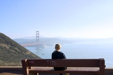 Güneşli bir günde, San Francisco, California 'daki Golden Gate Köprüsü' ne tek başına oturan birinin arka görüntüsü. 1 Aralık 2025