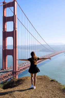 Uçurumun kenarında duran mutlu kadın gezgin, kolları açık, San Francisco, Kaliforniya 'daki Golden Gate Köprüsünün manzarasının keyfini çıkarıyor..