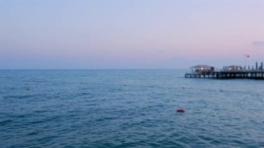 Akdeniz alacakaranlıkta sakin suyla pastel günbatımı gökyüzü ve uzak iskele