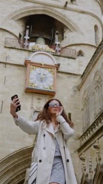 Bulutlu bir günde Bordeaux Fransa 'da tarihi taş saat kulesinin önünde poz verip selfie çeken bir kadın.