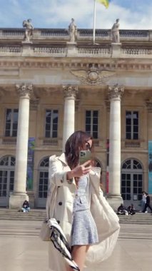 Bordeaux France 'lı kadın, güneşli bir günde 28 Mar 2025' te büyük neoklasik binaların önünde selfie çekerken poz veriyor.