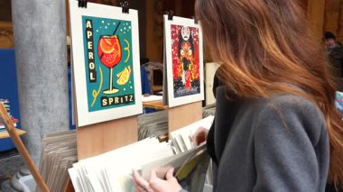 Vieille Bourse 'un Fransa' daki tarihi binasının avlusundaki market tezgahında antika posterleri ve sanat baskılarını karıştıran bir kadın.