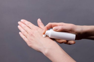 Kadın ellerine yakın plan beyaz şeker şişesinden cilde nemlendirici krem sürerek kişisel bakım ve hijyene odaklanıyor..
