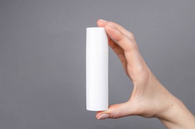 Kadınların elleri gri arka planda beyaz bir kozmetik kabı tutuyor. Cilt bakımına, güzelliğe ya da markalaşma sunumuna uygun..