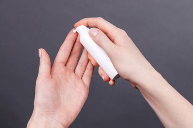 Kadın ellerine yakın plan beyaz şeker şişesinden cilde nemlendirici krem sürerek kişisel bakım ve hijyene odaklanıyor..