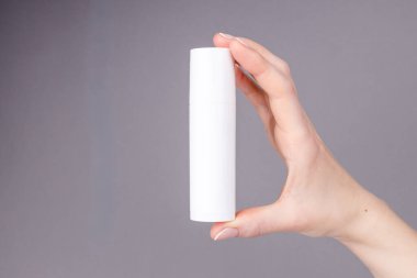 Kadınların elleri gri arka planda beyaz bir kozmetik kabı tutuyor. Cilt bakımına, güzelliğe ya da markalaşma sunumuna uygun..