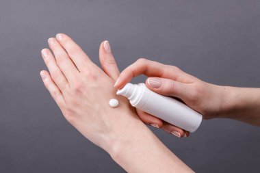 Kadın ellerine yakın plan beyaz şeker şişesinden cilde nemlendirici krem sürerek kişisel bakım ve hijyene odaklanıyor..