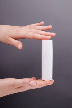 Kadınların elleri gri arka planda beyaz bir kozmetik kabı tutuyor. Cilt bakımına, güzelliğe ya da markalaşma sunumuna uygun..