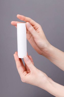 Kadınların elleri gri arka planda beyaz bir kozmetik kabı tutuyor. Cilt bakımına, güzelliğe ya da markalaşma sunumuna uygun..