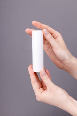 Kadınların elleri gri arka planda beyaz bir kozmetik kabı tutuyor. Cilt bakımına, güzelliğe ya da markalaşma sunumuna uygun..