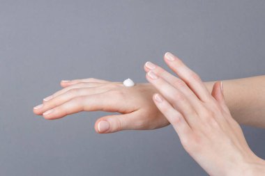 Kadın ellerinin cildine beyaz nemlendirici krem sürerken, cilt bakımını, su kaybını, yumuşaklığı ve kişisel bakım rutinini gösteren yakın çekim görüntüleri..