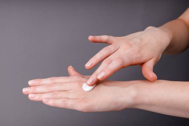 Kadın ellerinin cildine beyaz nemlendirici krem sürerken, cilt bakımını, su kaybını, yumuşaklığı ve kişisel bakım rutinini gösteren yakın çekim görüntüleri..