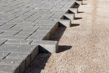 Gri beton kaldırım taşlarının çakıl temeline yerleştirilmesinin detaylı görüntüsü yüzey dokusunu ve inşaat sürecini gösteriyor. Yüksek kalite fotoğraf