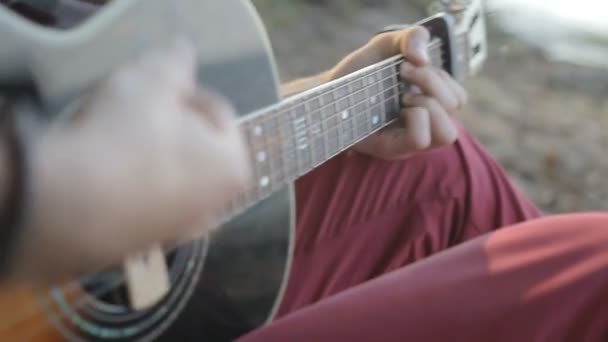A man plays the guitar while sitting by the sea. Close up — Stock Video