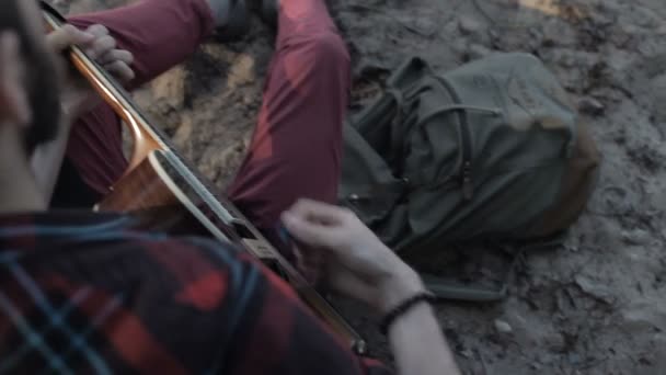 Чоловік грає на гітарі, сидячи біля моря — стокове відео