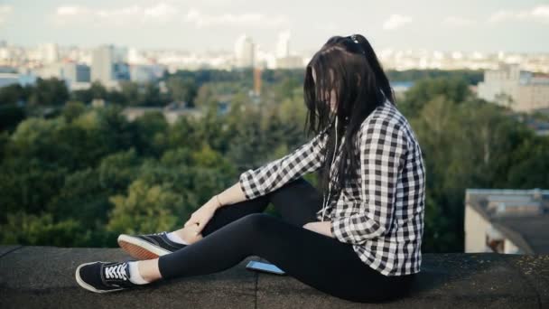 Chica escuchando música con auriculares en el techo — Vídeo de stock