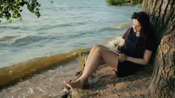 Mulher tomando notas em um caderno sentado na costa — Vídeo de Stock