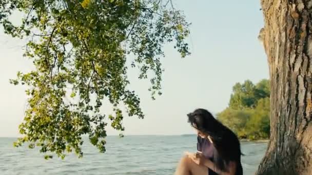 Girl reading a book sitting on the coast — Stock Video