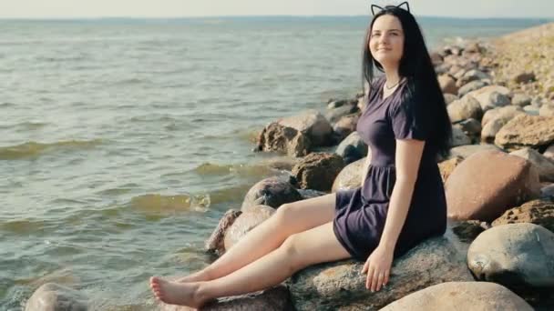 Chica sentada en rocas en la costa y posando — Vídeos de Stock
