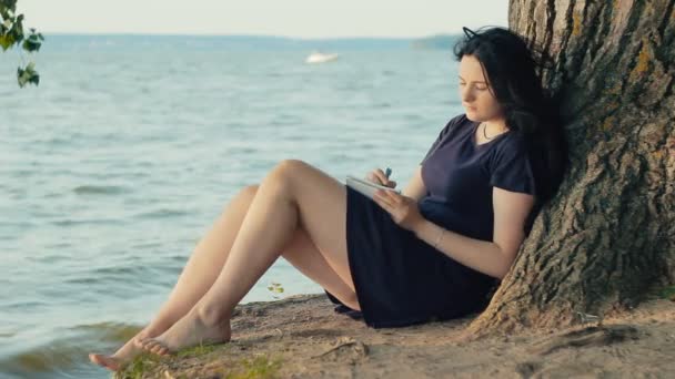 Mujer tomando notas en un cuaderno sentado en la costa — Vídeos de Stock