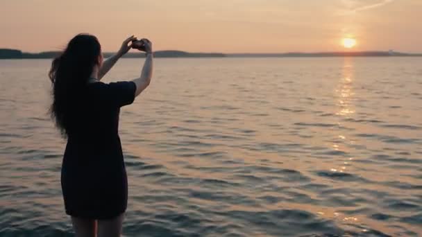 少女は、海岸に立って、夕日を撮影 — ストック動画