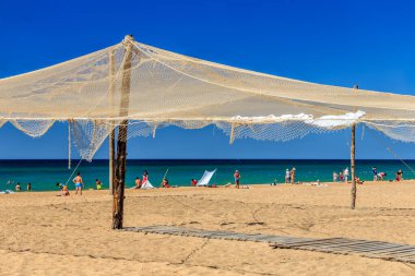 Sandy deniz kıyısı, süs olarak balıkçı ağları kullanılıyor. Güzel güneşli mavi gökyüzü manzarası. Karadeniz kıyısındaki Anapa tatil köyü. İnsanlar kıyıda dinleniyor
