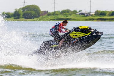 Krasnodar, Rusya - 25 Temmuz 2020: Nehir kıyısında günbatımında su sıçratan jet ski pilotu