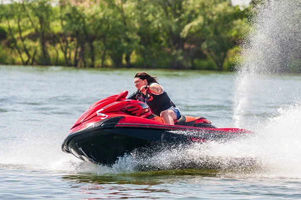 Krasnodar, Rusya - 25 Temmuz 2020: Genç mutlu Kafkasyalı kadın gün batımında kırsal kesimde nehir kıyısında jet ski sürüyor. Ekstrem sporlar ve aktif tatil kavramı