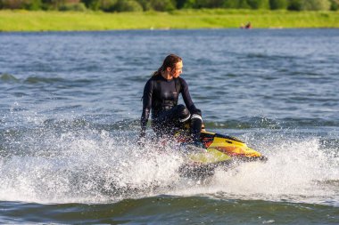 Krasnodar, Rusya - 25 Temmuz 2020: Genç Kafkasyalı jet ski kadın, gün batımında kırsal kesimde nehir kıyısında sıçramalar yaparak su aracını sürüyor. Güzel kadın süper jet sürücüsü serbest çalışıyor.
