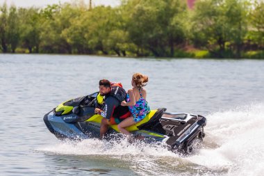 Krasnodar, Rusya - 25 Temmuz 2020: Arka koltukta mutlu bir kadınla erkek binici gün batımında kırsal kesimde nehir kıyısında su sıçrayan jet ski teknesi kullanıyor. Ekstrem sporlar ve yaz aktiviteleri konsepti