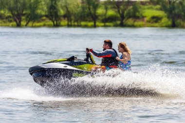 Krasnodar, Rusya - 25 Temmuz 2020: Arka koltukta mutlu bir kadınla erkek binici, gün batımında nehir kıyısında kırsal kesimde BRP Sea-Doo jet su aracını sürüyor. Ekstrem sporlar ve yaz aktiviteleri konsepti