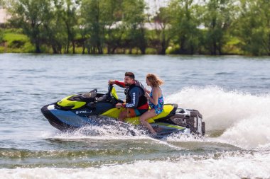 Krasnodar, Rusya - 25 Temmuz 2020: Arka koltukta mutlu bir kadınla erkek binici, gün batımında nehir kıyısında kırsal kesimde BRP Sea-Doo jet su aracını sürüyor. Ekstrem sporlar ve yaz aktiviteleri konsepti
